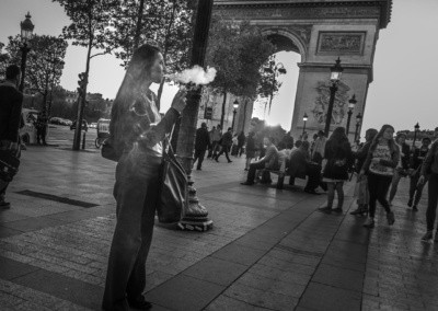 Photo shows a woman smoking a cigarette in front of the Arc de Triumphe in Paris