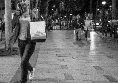 Photo shows a comparison of a young woman on her mobile phone holding a shopping bag, agains an elderly comple walking together on the Champs-Élysées