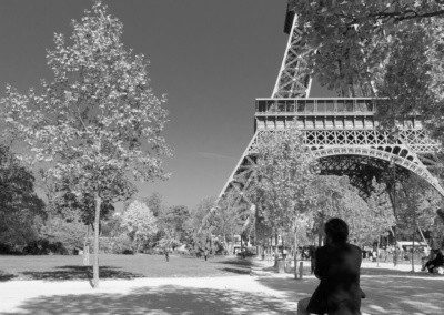 Photo shows a lone figure sitting on a rock gazing at the Eiffel Tower