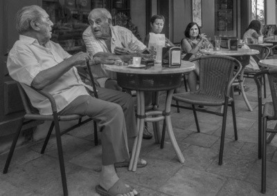 Photo shows two older men sitting at a café being looked at by two women.