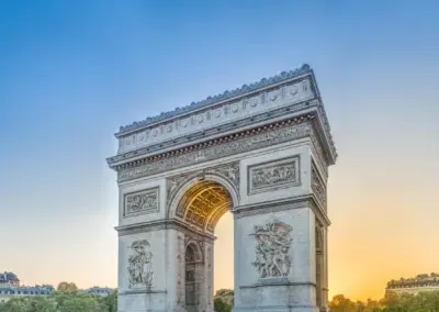 Photo of the Arc D'Triumph with the light of the setting sun streaming through the inside filling it with a warm glow of light balanced against the cool blue sky.
