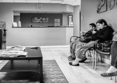 Photo of three people sitting in the dentist office looking at their phones while there is a widescreen TV right in front of them to look at.