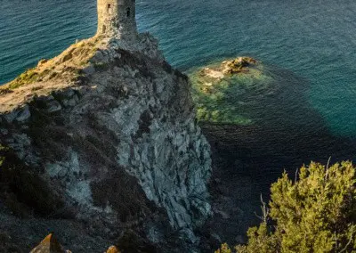 Photo shows a rustic stone tower positioned on a cliff overlooking the mediterranean sea as the sun sets.